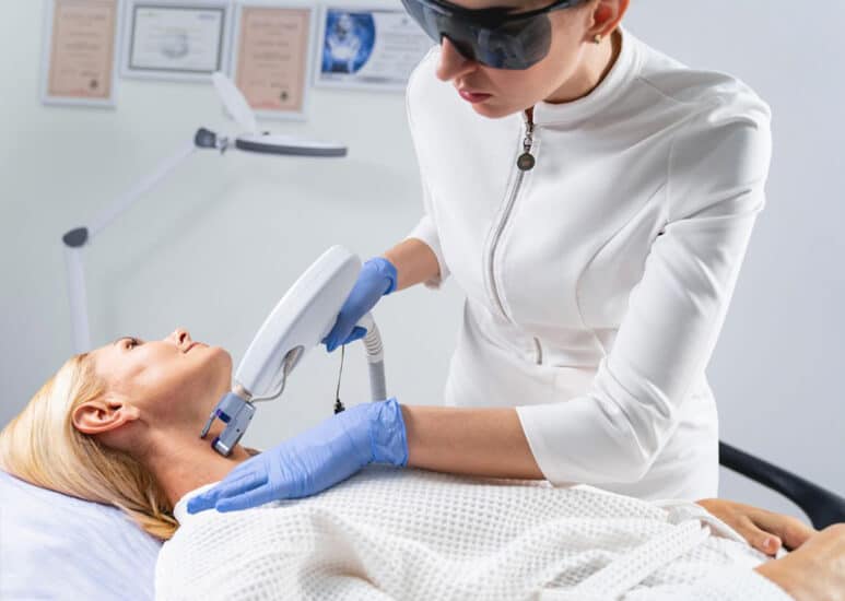 Esthetician performing radio-frequency skin tightening treatment on a client's neck and décolleté.